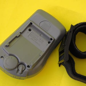 Puede incluir: Radio Sony SRF-M33 gris con correa negra, sobre fondo amarillo. La radio tiene un compartimento para pilas y un dial de control. La correa es de material negro suave.