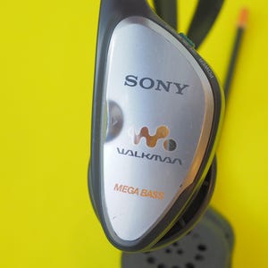 K&ouml;nnte beinhalten: Ein schwarzes und silbernes Sony Walkman-Headset mit dem Walkman-Logo und dem Schriftzug Mega Bass auf der Vorderseite. Das Ger&auml;t verf&uuml;gt &uuml;ber einen Netzschalter an der Seite und eine schwarze Antenne oben sowie eine runde Lautsprecherkomponente.