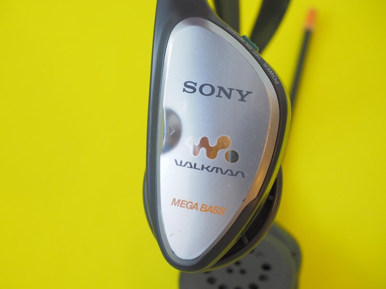 K&ouml;nnte beinhalten: Ein schwarzes und silbernes Sony Walkman-Headset mit dem Walkman-Logo und dem Schriftzug Mega Bass auf der Vorderseite. Das Ger&auml;t verf&uuml;gt &uuml;ber einen Netzschalter an der Seite und eine schwarze Antenne oben sowie eine runde Lautsprecherkomponente.