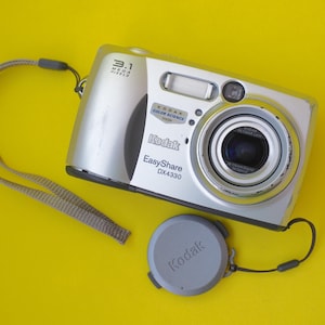May include: Silver Kodak EasyShare DX4330 digital camera with a lens cap and a beige wrist strap. The camera has a 3.1 megapixel resolution and the Kodak Color Science logo.