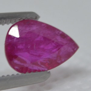 Puede incluir: Una piedra preciosa rosa en forma de pera sostenida en unas pinzas.