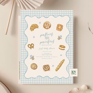 May include: A baby shower invitation with a light blue gingham border and a cream-colored interior. The invitation features watercolor illustrations of pastries, pacifiers, and the text "pastries and pacifiers". The invitation is for a baby shower.