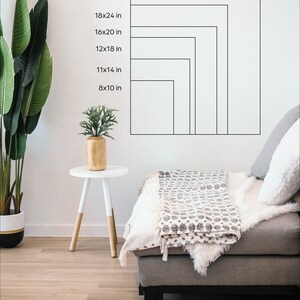 May include: A white wall with a series of black outlines showing different sizes of rectangular frames. The measurements of each frame are listed in inches. The frames are shown on a white wall in a living room setting with a couch and a side table.