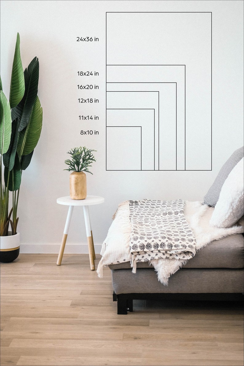 May include: A white wall with a series of black outlines showing different sizes of rectangular frames. The measurements of each frame are listed in inches. The frames are shown on a white wall in a living room setting with a couch and a side table.