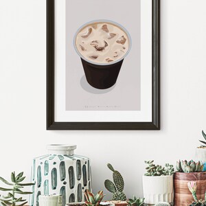 May include: A framed illustration of a glass of iced latte with the text "ICED LATTE" above the glass. The illustration is on a light gray background. The frame is black and the glass is clear with a brown liquid and ice cubes inside.