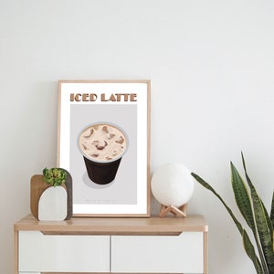May include: A framed print with the text "ICED LATTE" in brown letters. The print features a cartoon illustration of a cup of iced coffee with ice cubes.