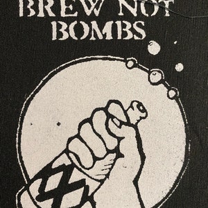 May include: Black and white patch with the text "Brew Not Bombs" and a graphic of a hand holding a bottle with a label that has a crosshatch pattern.