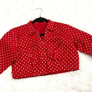 May include: A red and gold brocade blouse with a collared neckline and three-quarter sleeves. The blouse has a fitted bodice and a cropped length.