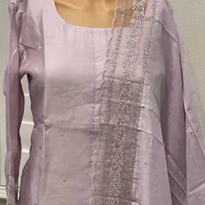 May include: A lilac-colored long-sleeved dress with a sheer lace trim. The dress has a scoop neckline and a straight silhouette.