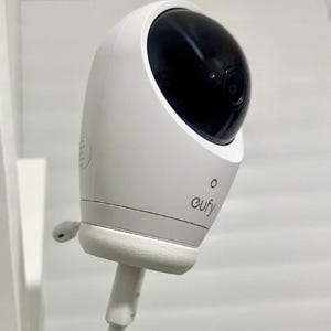 以下が含まれることがあります： 丸みを帯びたマットホワイトの本体と、光沢のある黒い球状のレンズハウジングを備えた白いセキュリティカメラ。デバイスの前面にはグレーでeufyというブランド名が印刷されており、小さな円形のインジケーターライトと白い電源ケーブルが接続されています。