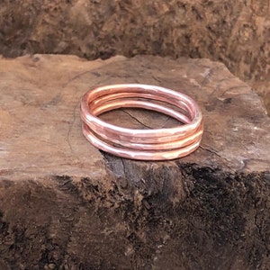 May include: Three hammered copper rings stacked on top of each other. The rings are a light rose gold color.