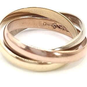 Peut inclure: Une bague à trois anneaux en or jaune, or rose et or blanc. Les anneaux sont entrelacés, créant un design classique. La bague est posée sur un fond blanc, mettant en valeur ses couleurs et ses détails. Un bijou intemporel.