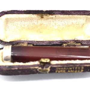 Könnte beinhalten: Ein brauner Bernstein-Zigarettenhalter in einem braunen Lederetui mit den Worten "Guaranteed Pure Amber" auf der Unterseite.