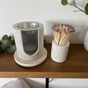 May include: A marble-effect oil burner with a silver bowl and a matching cylindrical match holder filled with matches. The burner sits on a decorative base. The matches have purple tips.