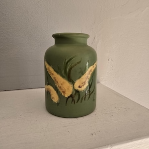 May include: A green ceramic vase with a hand-painted design of yellow flowers. The vase has a rounded body and a slightly flared lip.