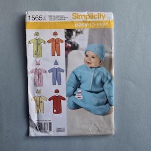 May include: Simplicity sewing pattern 1565A for baby sleepwear. The pattern features various designs, including a bunny, moon, and star, with a baby wearing a blue sleepsuit and hat. The pattern is easy-to-sew.