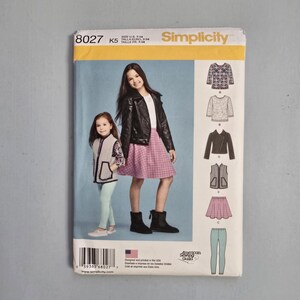 May include: Simplicity sewing pattern envelope featuring two young girls modeling clothing. The pattern includes designs for a jacket, vest, skirt, and pants. The envelope is white and blue with the pattern number 8027.