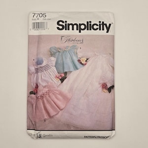 May include: Simplicity sewing pattern 7705, size A (NB-12M). The pattern features a classic heirloom design for baby clothes. The cover shows examples of the finished garments in white, pink, and blue, with floral accents.
