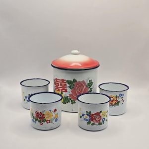 May include: A white enamelware set consisting of a lidded canister and four matching mugs. Each piece features a floral pattern with red, yellow, and blue flowers, and the canister displays a red Chinese double happiness character symbol.