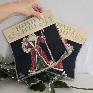 May include: Two square tapestry patches featuring Santa Claus in a red and green robe, holding a staff and flowers, on a black background. The top of each patch has the text "The Tapestry Patch" in green. The patches are approximately 9x9 inches.