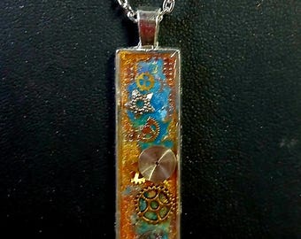 May include: A rectangular pendant necklace with a silver chain. The pendant features a steampunk design with gears, blue and gold accents, and a silver bezel. The background is a mix of orange and blue.