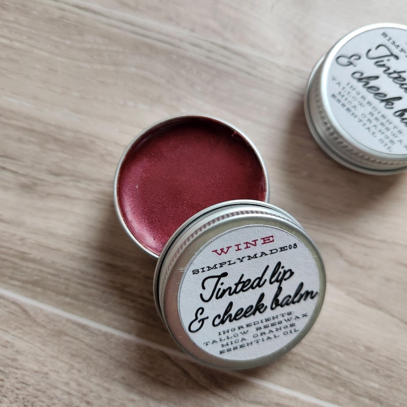 May include: A small tin of tinted lip and cheek balm in the color wine. The label reads "Wine Simply Made 08 Tinted Lip & Cheek Balm" and lists the ingredients: Tallow Beeswax, Mica Orange, Essential Oil.