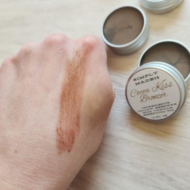 Cream bronzer in a metal tin made with grass fed tallow and beeswax.  The bronzer is swatched on a hand and contains a warm glowing shimmer.