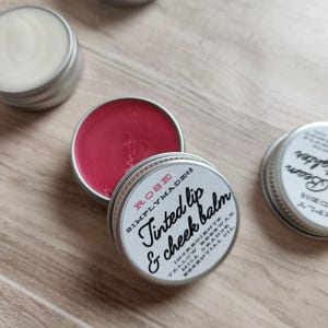 May include: A small tin of rose-tinted lip and cheek balm with the label "ROSE SIMPLYMADE08 Tinted lip & cheek balm INGREDIENTS:  TALLOW BEESWAX  MICA ORANGE  ESSENTIAL OIL"