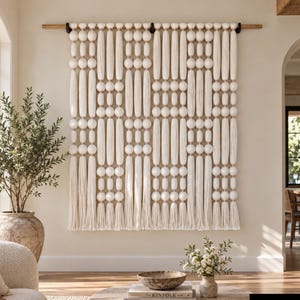 May include: A large off-white wall hanging featuring a repeating pattern of vertical fiber columns and spherical beads suspended from a wooden rod. The textile art piece displays a structured arrangement of long, straight strands and round elements.