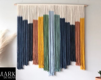 May include: A colorful macrame wall hanging with a geometric design. The hanging features shades of blue, green, yellow, and orange yarn.