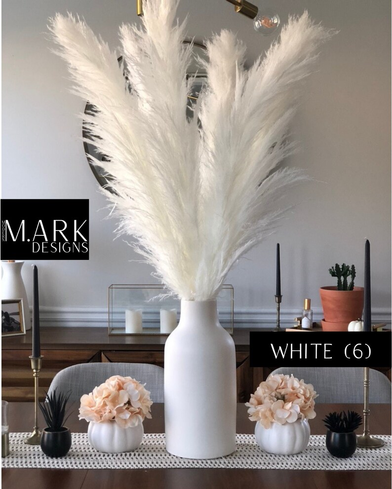 May include: White pampas grass in a white ceramic vase with two smaller white ceramic vases with peach colored flowers. The text "WHITE (6)" is visible in the image.