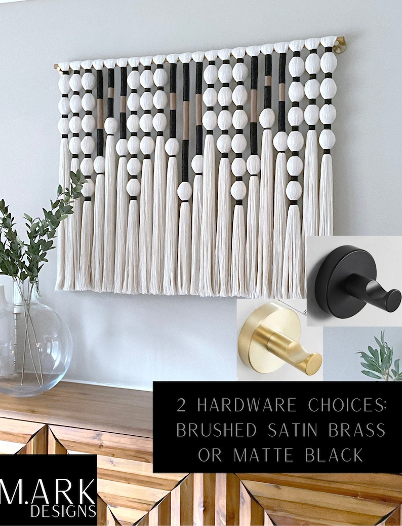 K&ouml;nnte beinhalten: Ein wei&szlig;er, schwarzer und beigefarbener Makramee-Wandbehang mit einem Holzstab und Quasten. Zwei Optionen f&uuml;r Wandhaken werden gezeigt: geb&uuml;rstetes Satin-Messing und mattschwarz. "2 Hardware Choices: Brushed Satin Brass or Matte Black" steht in schwarzer Schrift auf wei&szlig;em Hintergrund.