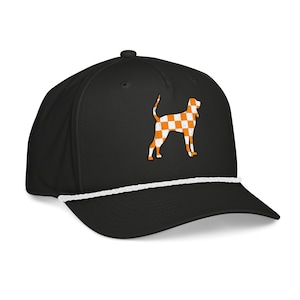 Könnte beinhalten: Schwarze Baseballkappe mit weißem Seildetail und gebogenem Schirm. Die Kappe zeigt eine karierte orange-weiß Hundesilhouette auf der Vorderseite. Ein stilvolles Accessoire für Hundeliebhaber.