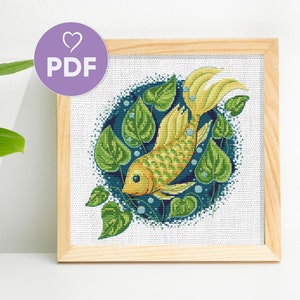 Könnte beinhalten: Ein Kreuzstichmuster mit einem gelben Fisch, der in einem Kreis aus grünen Blättern und blauen Blasen schwimmt. Das Muster ist in einem hellen Holzrahmen gerahmt.