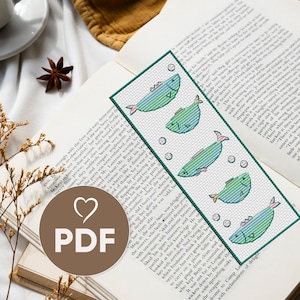 May include: A cross-stitch bookmark featuring a white background with five blue and green fish swimming in a row. The fish are outlined in black and have small pink bubbles around them. The bookmark is bordered in green.