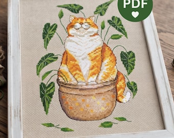 May include: A cross-stitch embroidery in a white frame featuring an orange and white tabby cat sitting inside a brown ceramic pot, surrounded by green leafy plants on a beige fabric background. The image includes a green circular PDF icon.