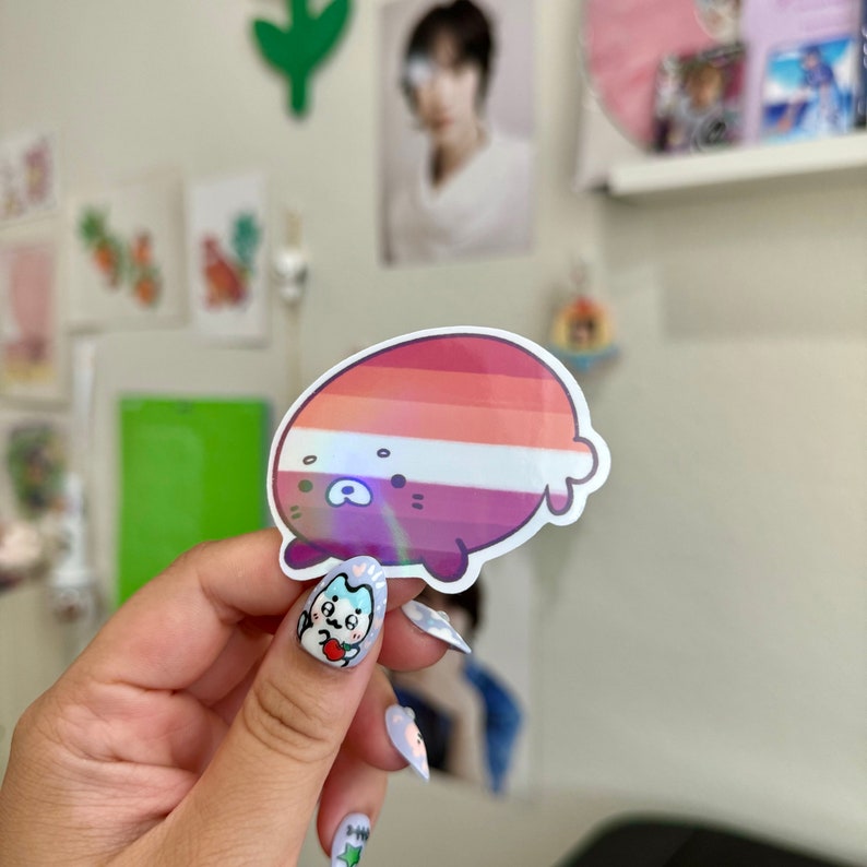 May include: A holographic sticker of a cartoon animal with a pink, white, and red striped pattern. The animal is lying on its side with its head turned to the side.