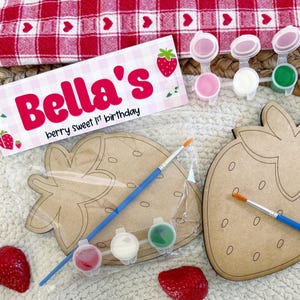 May include: A craft kit featuring strawberry-shaped wooden cutouts, paint pots, and paintbrushes. The kit includes a sign that reads "Bella's berry sweet 1st birthday." The kit includes three paint colors.