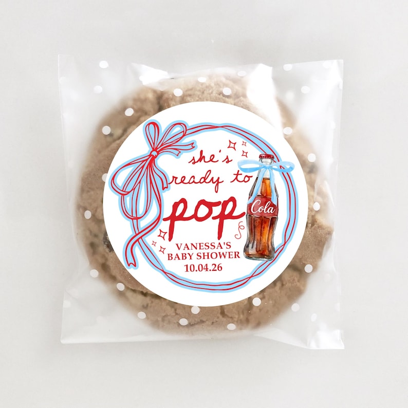 Pu&ograve; includere: Un biscotto con gocce di cioccolato in un sacchetto di cellophane trasparente con pois bianchi. Il biscotto ha un adesivo circolare con il testo "she's ready to pop" e un'illustrazione di una bottiglia di cola vintage. L'adesivo include anche il testo "VANESSA'S BABY SHOWER 10.04.26".