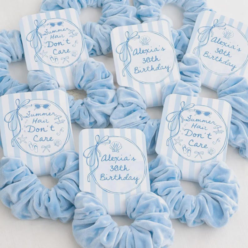 Op de afbeelding: Lichtblauwe fluwelen scrunchies met bijpassende kaarten. De kaarten tonen de teksten "Summer Hair Don't Care" en "Alexia's 30th Birthday" in een cirkel, met strandthema-illustraties, op een blauw-wit gestreepte achtergrond.