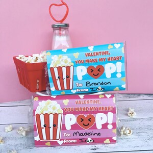 May include: Two Valentine's Day popcorn treat bags with the text "VALENTINE, YOU MAKE MY HEART POP!" and a cute popcorn graphic. One is addressed to Brandon, the other to Madeline. A red basket of popcorn and a heart-shaped straw are also visible.