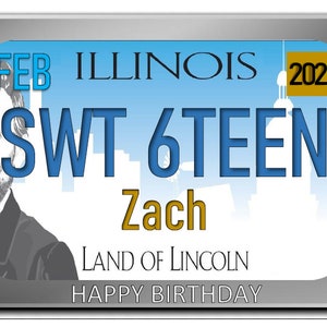 May include: A blue and white Illinois license plate with the text "SWT 6TEEN Zach" and "LAND OF LINCOLN HAPPY BIRTHDAY". The plate has a silver border and a gold 2020 sticker in the top right corner.