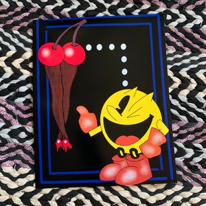 May include: A Pac-Man themed art print featuring the iconic yellow character with red boots and gloves, and a pair of cherries. The artwork is set against a black background with a blue border.