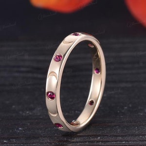 May include: A thin gold band ring with a textured surface and small red gemstones set into the band.