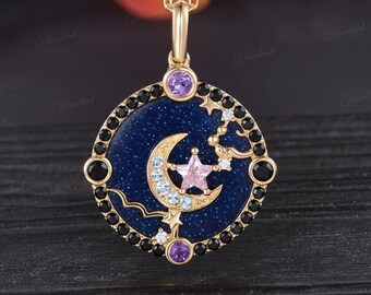 May include: Gold-tone necklace with a circular pendant featuring a blue speckled background, a crescent moon, and a pink star. The pendant is adorned with black and clear gemstones, and the chain is gold. The word "Moonland" is at the bottom.