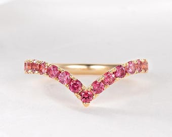 Puede incluir: Un delicado anillo de banda de oro con un diseño en forma de V engastado con zafiros rosas.