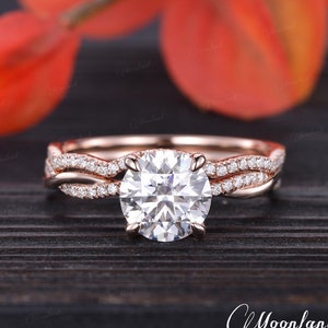 May include: A rose gold engagement ring with a round brilliant cut diamond center stone and a pave diamond band. The ring features a twisted band design.