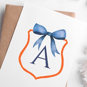 May include: A watercolour illustration featuring a white shield with an orange border, a blue bow, and the letter "A". The artwork is set against a white backdrop, with a brown envelope and decorative elements.