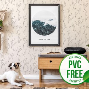Puede incluir: Un papel tapiz beige con un delicado patrón de flores dibujado con líneas. El papel tapiz es libre de PVC y está certificado. Un perro está acostado en el suelo frente a la pared. Un banco de madera con un cojín negro está frente a la pared. Una impresión enmarcada con una foto de un bosque y el texto "Follow The Flow" está colgada en la pared. Una planta en maceta está en el lado derecho de la imagen.