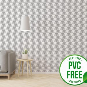 Puede incluir: Un papel tapiz con un patrón geométrico gris y blanco con un sofá gris y una pequeña planta sobre una mesa de madera delante de él. Una hoja verde con un círculo blanco con el texto "CERTIFIED PVC FREE CERTIFIED" está en la esquina inferior derecha de la imagen.